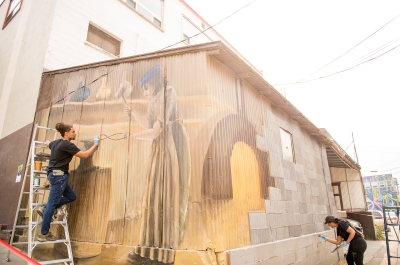 Two artists painting a mural during the Nelson International Mural Festival