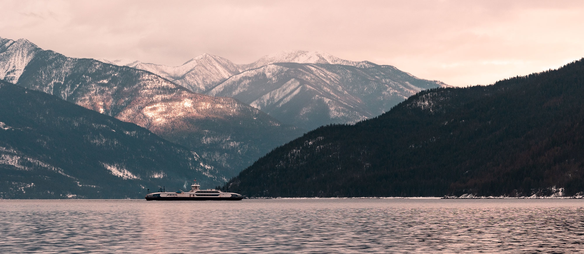 Kootenay Lake Ferry on the water with snowcapped mountains in background.