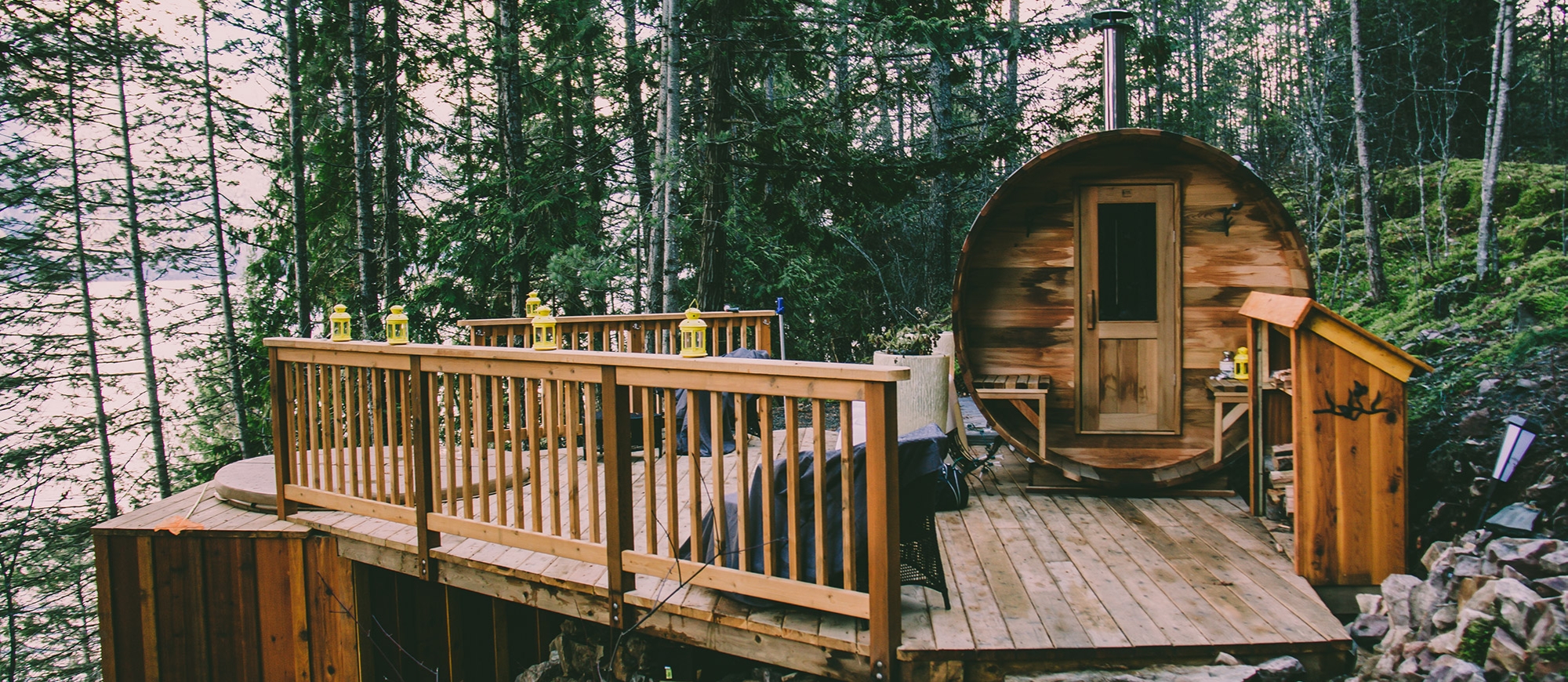 A cylindrical cabin next to a hot tub set into a wooden deck, overlooking Kootenay Lake