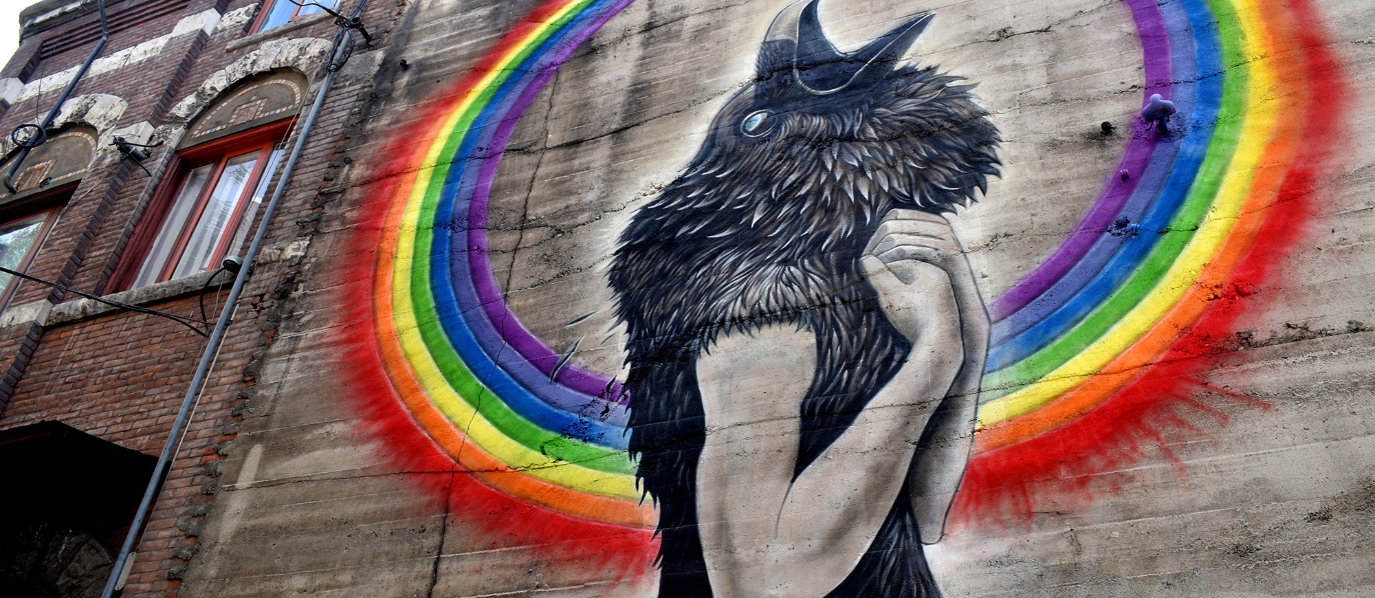 A mural  of a black bird head on a human's body from the Nelson BC Mural Festival