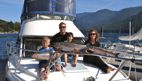 A mom, dad and two children hold up the fish they've caught on a Kootenay Wild Fishing Charter boat