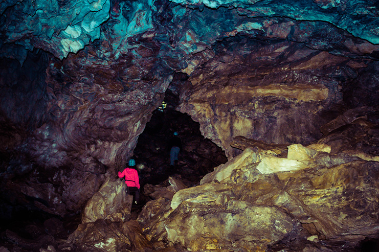 A woman facing away and into a dark expanse within a cave