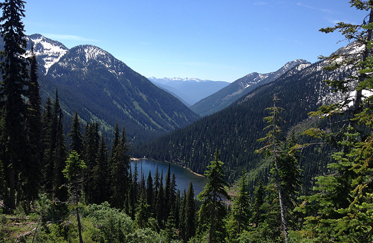 A small lake, viewed from above, nestled within several tall mountains on a sunny summer day