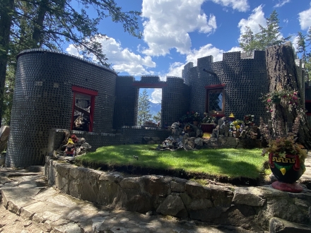 A castle-like house made out of glass bottles with green grass and lawn gnomes around it.