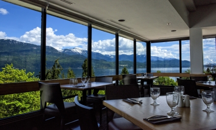 Fine dining tables which are set with wine glasses and cutlery. The sky and mountains can be seen through the glass windows