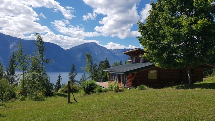 A wood cottage with a green lawn and lake view.