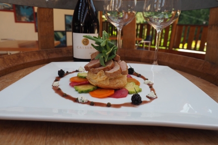 A plate of delicious looking food with two wine glasses and a bottle of red wine