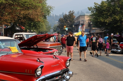 A red car in the foreground with people walking around enjoying the Queen City Car Show in Nelson. Photo by Janelle Lewchuk.