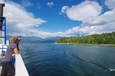 Two people on a ferry looking over the side at the lake on a sunny day, enjoying things to do near Nelson BC