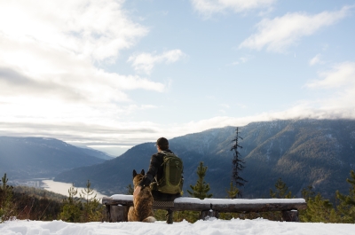 A hiker sitting on a bench next to his dog whilst looking out onto Kootenay Lake.