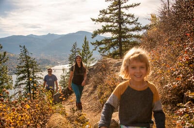 A family hiking Lyon's Bluff in Nelson BC with a view of Kootenay Lake and the big orange bridge in the background.