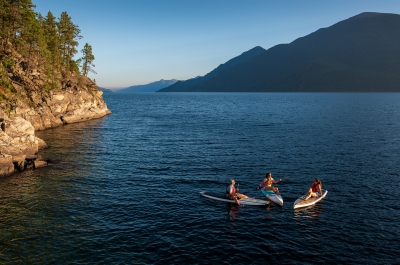 Three paddle boarders sitting on their boards facing each other on Kootenay Lake, BC