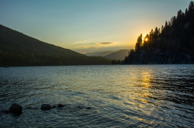 The sun setting behind trees on the shore of Kootenay Lake