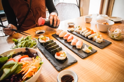 Hands pouirng soy sauce into a small dish with a table full of colourful sushi.