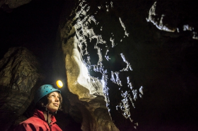 A person with a helmet and headlamp on looking up at a wall inside Cody Caves, near Nelson BC