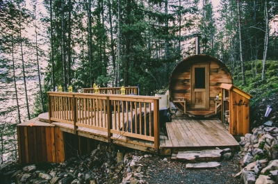 A cylindrical cabin next to a hot tub set into a wooden deck, overlooking Kootenay Lake