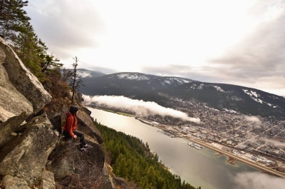 A woman sitting on pulpit rock, looking down on Nelson BC far below