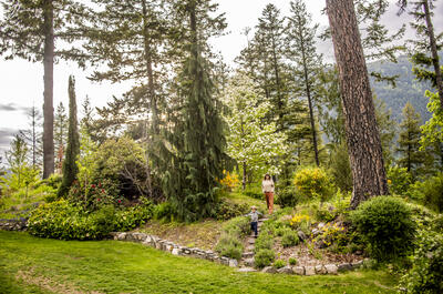 A mother and her toddler son, walking through a park with flowers blooming in Nelson BC's Gyro Park.