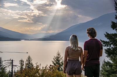 A couple looking out over Kootenay Lake with a ferry riding along the water.