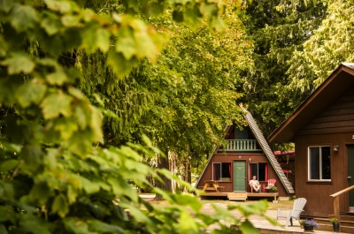 Cabins with green and red details, hidden amongst the trees, with a person lounging on the deck.