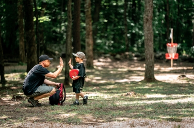 Man giving a high 5 to a small child at a disc golf course