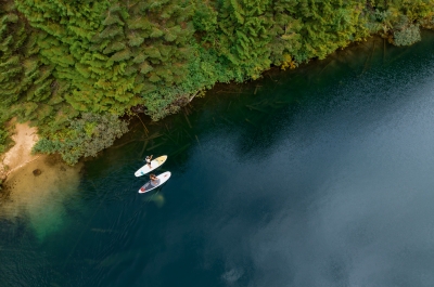 Two people on stand up paddle boards, paddling along the shoreline of Cottonwood Lake.