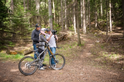 Two filmers reviewing footage off of a camera with a mountain biker