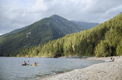 Kayakers and people on the beach with mountains in the backcountry at Lockhart Beach Provincial Park near Crawford Bay, BC