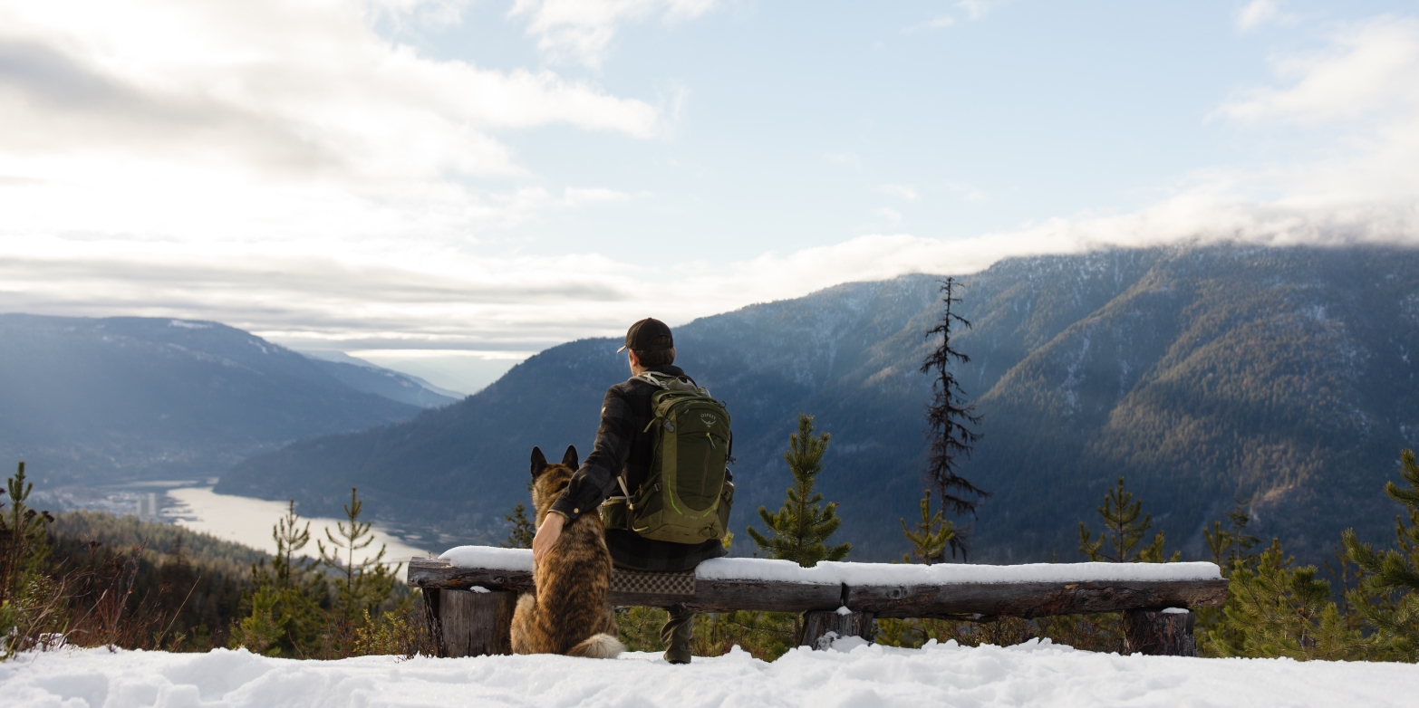 A hiker sitting on a bench next to his dog whilst looking out onto Kootenay Lake.