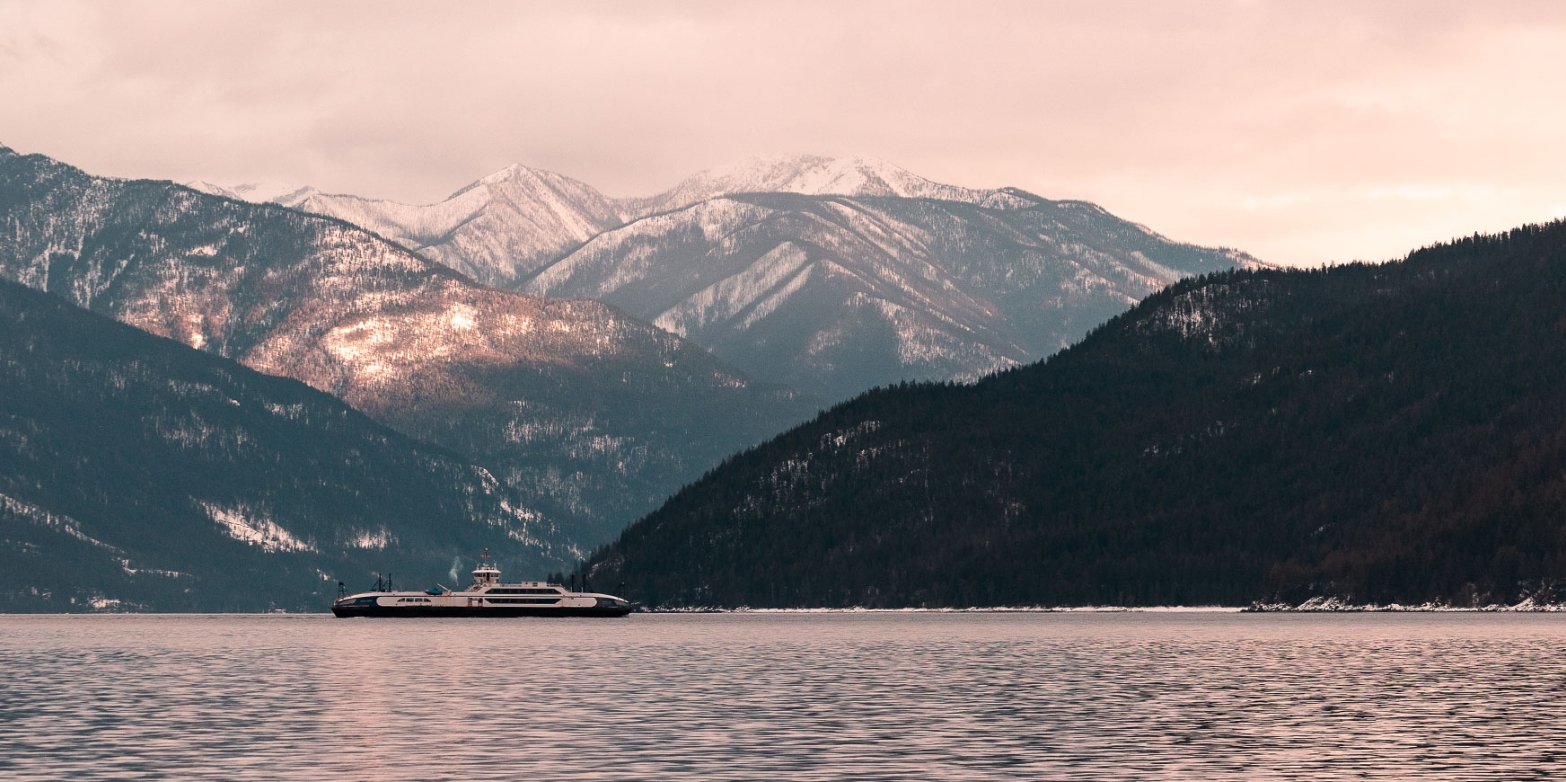 Kootenay Lake Ferry on the water with snowcapped mountains in background.