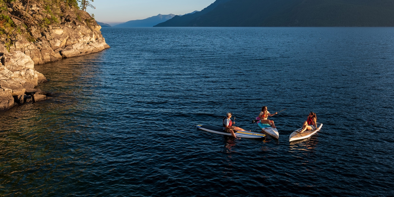 Three paddle boarders sitting on their boards facing each other on Kootenay Lake, BC