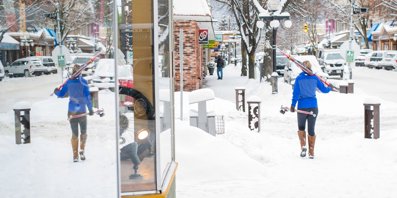 Woman walking downtown Nelson BC carrying cross country skis