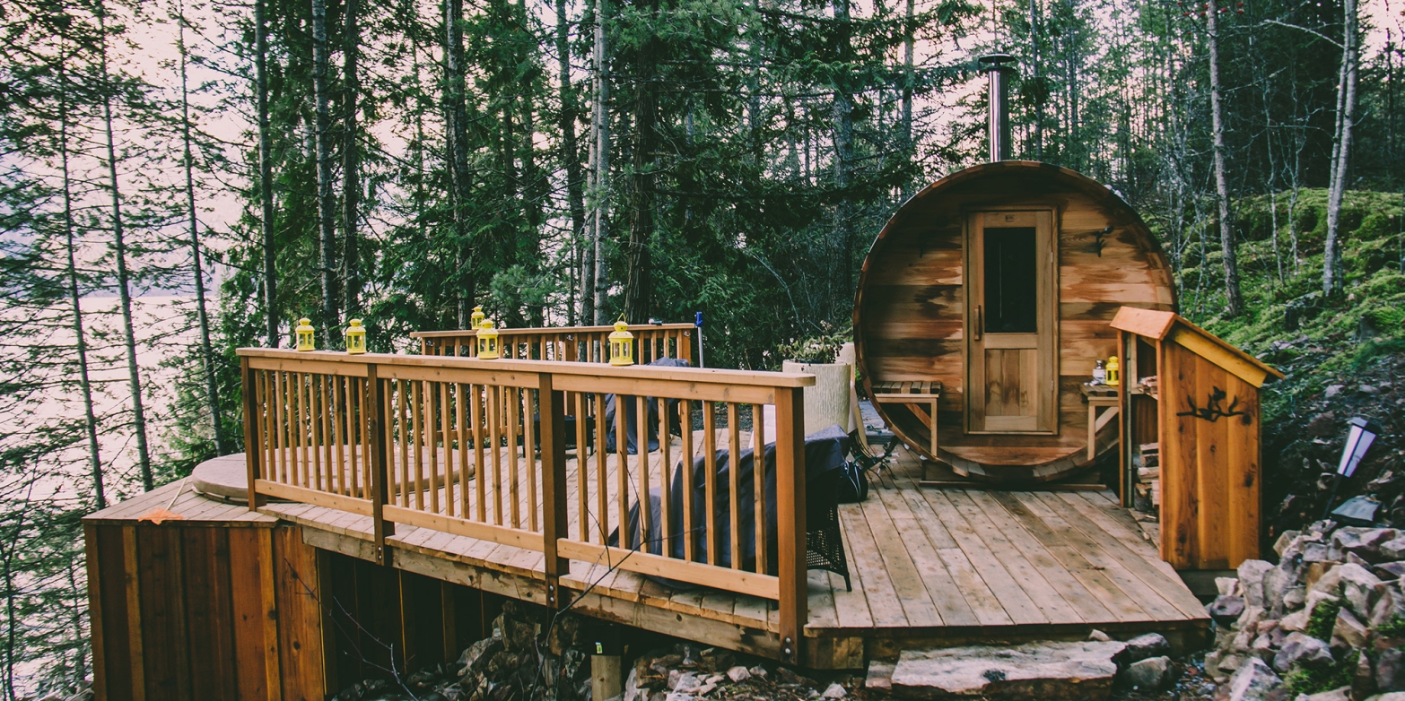 A cylindrical cabin next to a hot tub set into a wooden deck, overlooking Kootenay Lake