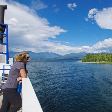 Two people on a ferry looking over the side at the lake on a sunny day, enjoying things to do near Nelson BC