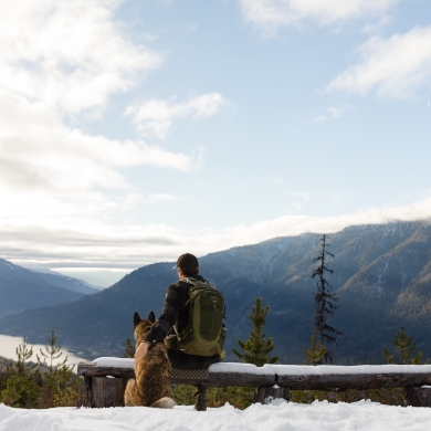 A hiker sitting on a bench next to his dog whilst looking out onto Kootenay Lake.
