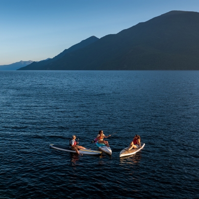 Three paddle boarders sitting on their boards facing each other on Kootenay Lake, BC