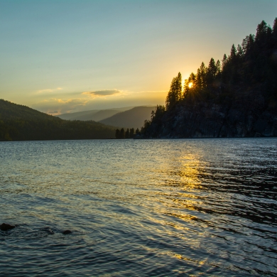 The sun setting behind trees on the shore of Kootenay Lake