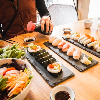 Hands pouirng soy sauce into a small dish with a table full of colourful sushi.