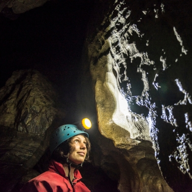 A person with a helmet and headlamp on looking up at a wall inside Cody Caves, near Nelson BC