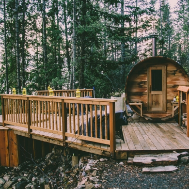 A cylindrical cabin next to a hot tub set into a wooden deck, overlooking Kootenay Lake