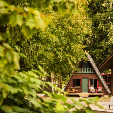 Cabins with green and red details, hidden amongst the trees, with a person lounging on the deck.