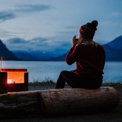 A girl sitting by a campfire on the shores of Kootenay Lake, BC.