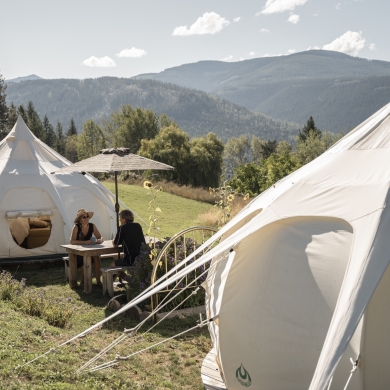 Two people sitting at a picnic table surrounded by mountains and glamping tents.