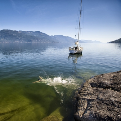 Jumping into Kootenay Lake with a sailboat in the background. 