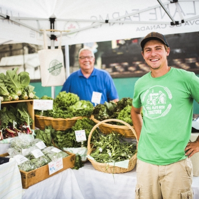 A farmer stands with a table full of produce at the Nelson Downtown Market