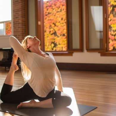 Someone doing yoga in a Nelson, BC studio with vibrant fall colours in the windows.