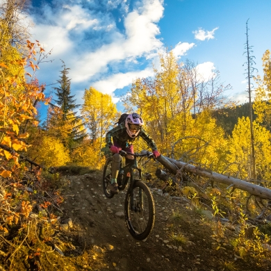 A person riding down a steep mountain bike trail surrounded by vibrant fall colours.