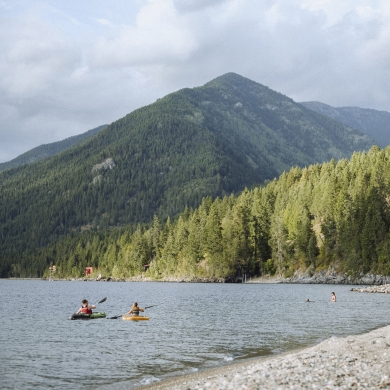 Kayakers and people on the beach with mountains in the backcountry at Lockhart Beach Provincial Park near Crawford Bay, BC