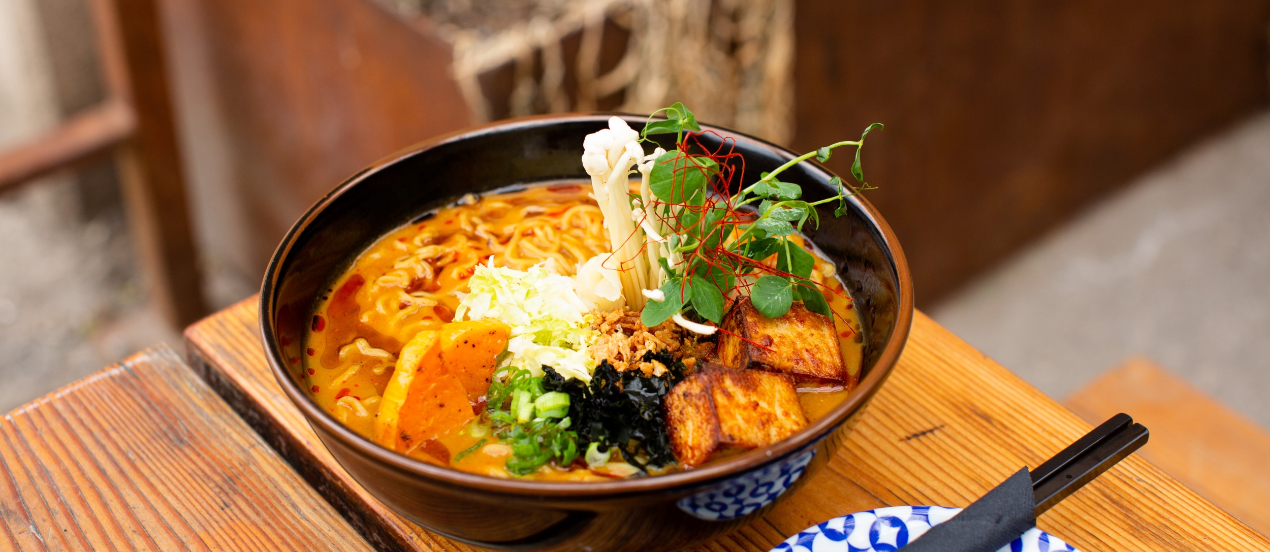 Bowl of Butternut Miso Tofu Ramen on a Patio Table With Chopsticks.