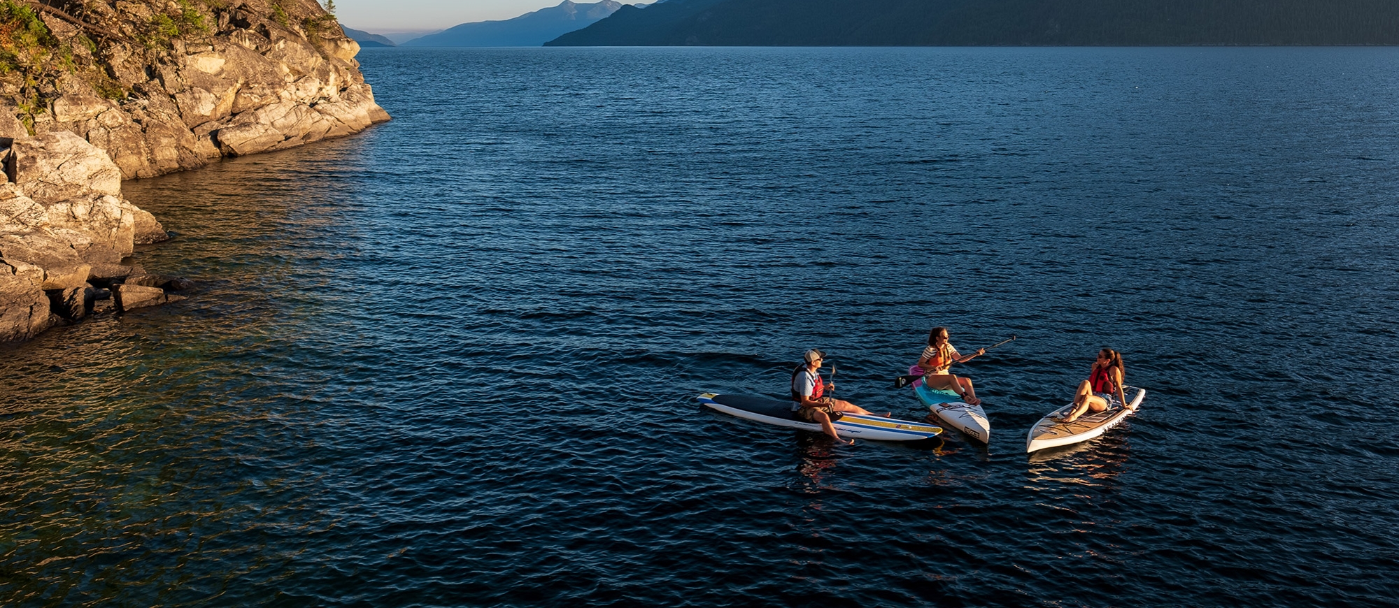 Three paddle boarders sitting on their boards facing each other on Kootenay Lake, BC